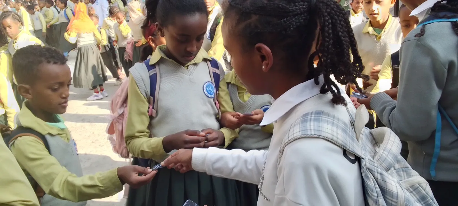 A student volunteer handing an FHI health card to a young boy in a crowded schoolyard