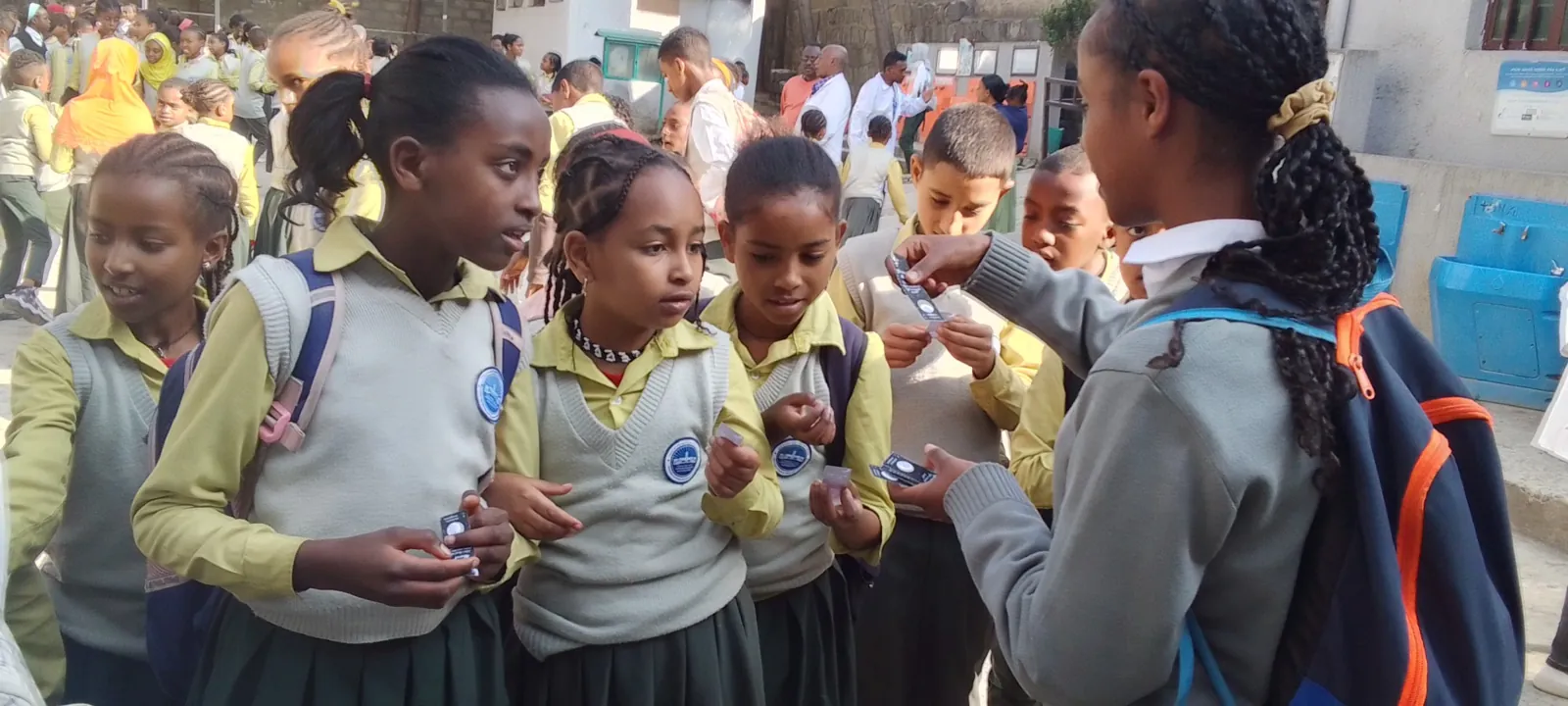 School children in uniform crowding around a student volunteer handing out FHI health cards