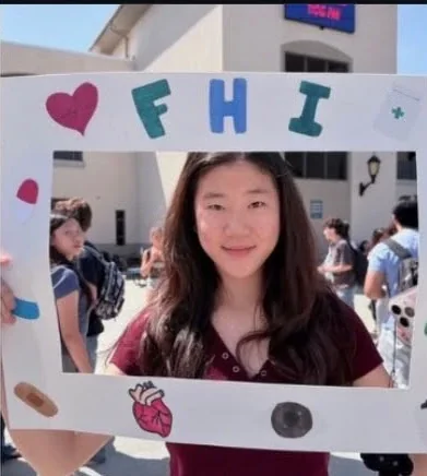 Students posing behind FHI's hand-decorated photo frame at a school fair