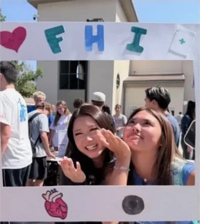 Students posing behind FHI's hand-decorated photo frame at a school fair