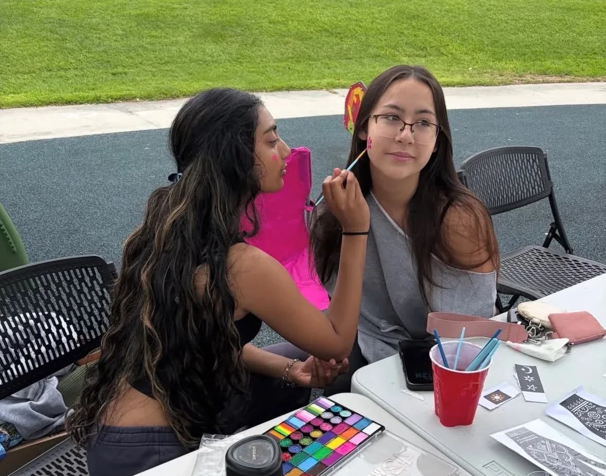 A volunteer painting a small design on a student's cheek at an outdoor fundraiser table