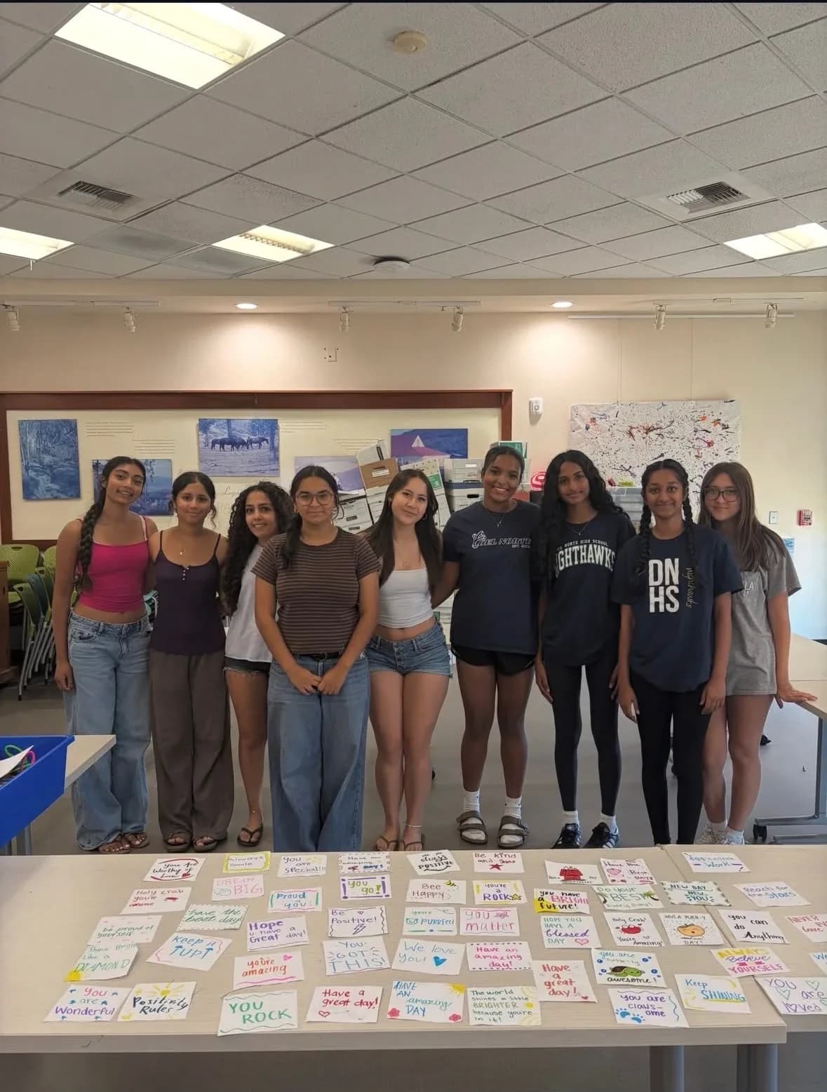 Nine volunteers standing behind a table covered in handwritten notes of encouragement