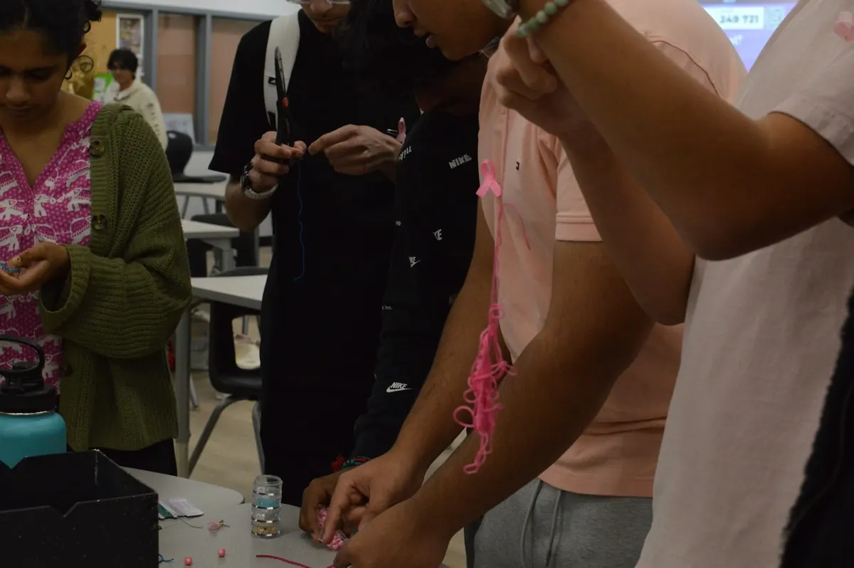 Students threading pink bracelets around a table