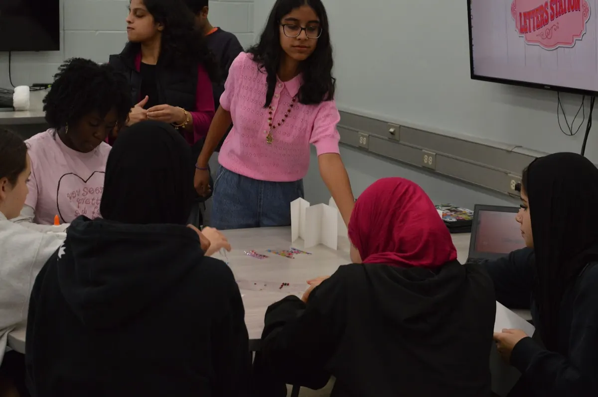 A volunteer in pink running the letters station while students write cards
