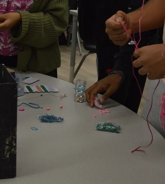 Hands threading beads onto pink bracelets at a craft table