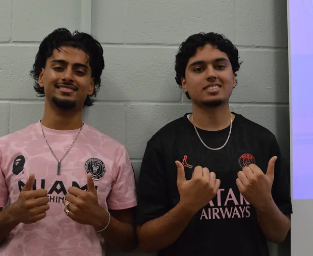 Two students in pink shirts giving a thumbs up at FHI's breast cancer awareness event