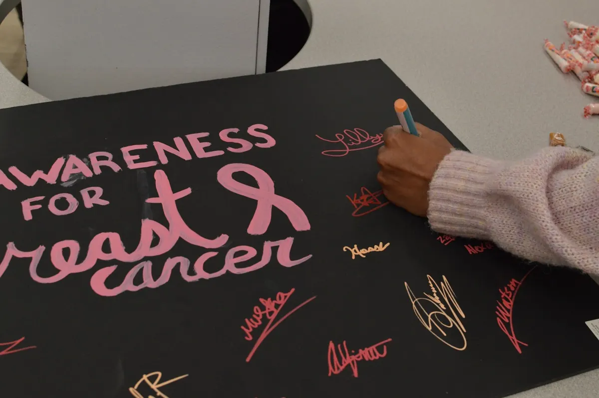 A student signing a black Awareness for Breast Cancer poster in pink marker