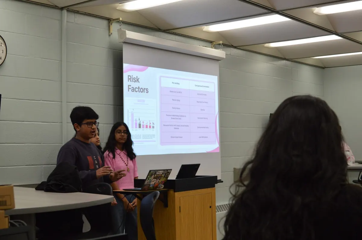 Two student presenters at a podium in front of a Risk Factors slide