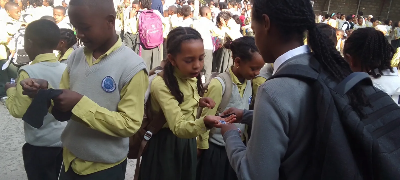 A student volunteer placing an FHI health card in a girl's hand as classmates look on