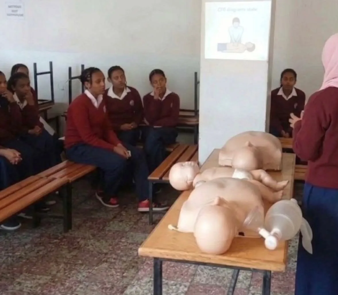 Students in school uniforms watching a CPR demonstration with adult and infant training manikins
